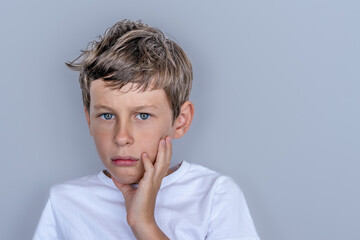 A white Eastern European 9-year-old boy in a white t-shirt looks directly at the camera and holds his hand in front of his face.