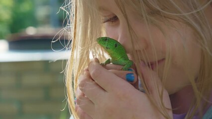 a little girl holding a small green lizard in her hands and kisses . lizards catch beetles, butterflies and other crop pests, feed on bears, which helps gardeners and farmers. an unusual pet. 