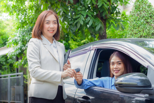 Beautiful young woman car salesman holding car keys and handing it to Asian female customer.