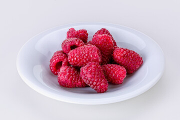 White saucer full of ripe large raspberries