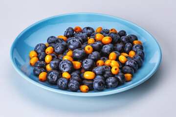 Blue plate with ripe blueberries and sea buckthorn berries on a white background