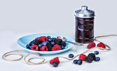 Fresh summer berries in a blue plate with a teaspoon and on the table, next to a jar of ready-made jam