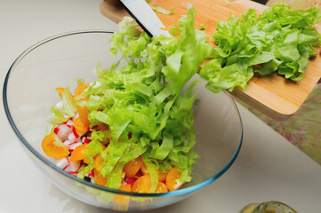 salad with greens, tomatoes and radishes in a glass bowl. sliced lettuce on a board with a knife, top view