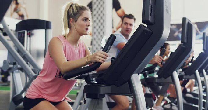 Fit, active and healthy woman cycling on exercise bike in gym workout, training and fitness class with group of people. Serious, athletic and sporty athlete using machine equipment for cardio health