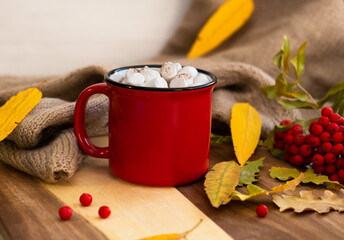 Red mug of cocoa, yellow leaves and cinnamon, on a light background. Autumn concept