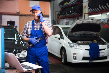 Auto mechanic with laptop talking on mobile phone in auto repair shop