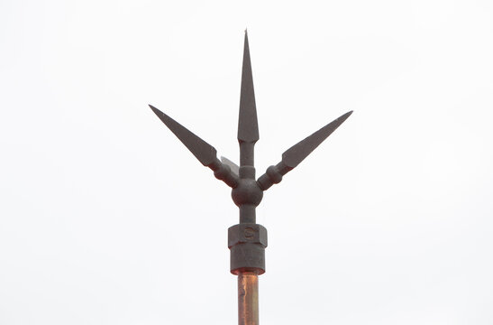 Lightning rod with three sharp metallic spikes mounted on a copper pole, designed for efficient lightning protection. Captured against a bright sky background, lightning protection