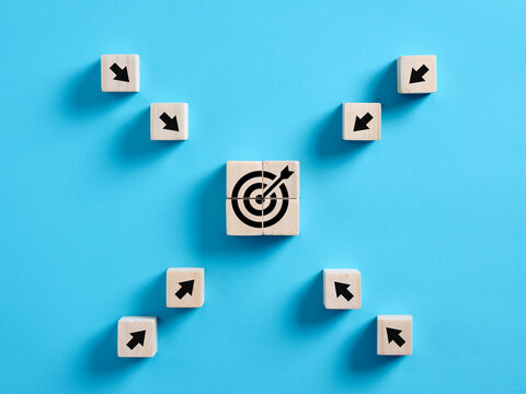 Arrows pointing towards the target icon on wooden cube. Achieving goals or aiming and focusing on the target in business