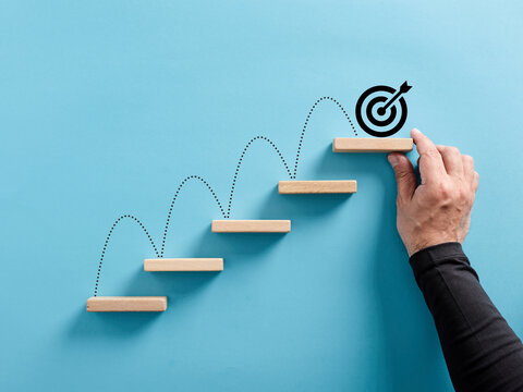 Male hand arranges a wooden block staircase with target icon. Achieving goals and objectives or goal setting