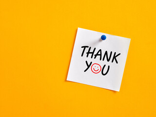 The word thank you written on a note paper pinned on a yellow board.