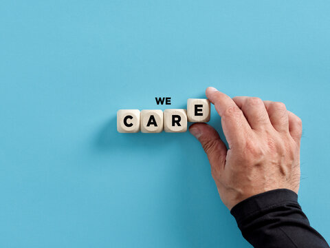 Male hand arranging wooden cubes with the word we care. Giving care, support, assistance, help and providing the needs