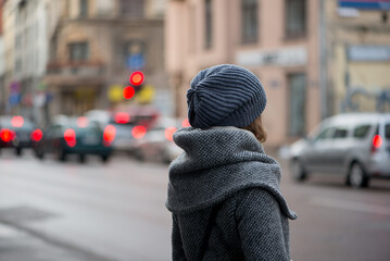 Rear view of a young woman in autumn clothes, who is standing in a small street, blurred traffic background