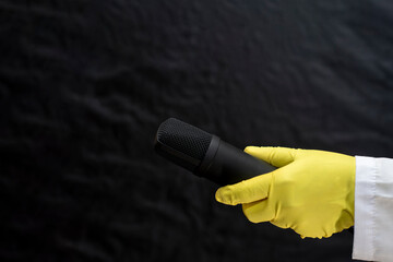 A doctor in a medical gown and protective gloves holds a microphone. The face is not visible. The...