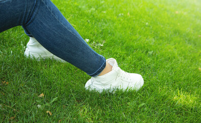 Young woman wearing stylish sneakers on green grass.