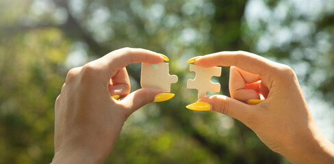 Woman holding a piece of wooden jigsaw puzzle together in the outdoors.