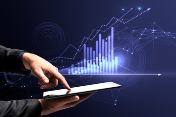 Close up of businessman hand pointing at tablet with abstract glowing polygonal business graph hologram with growing arrow on blurry background. Financial growth, market and trade concept.