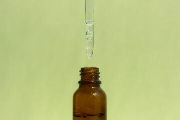 A bottle of dark amber glass with a serum or gel with a pipette on a green background. Cosmetic product with hyaluronic acid. Front view.