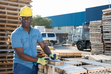 African-american builder filling documentation while standing beside concrete hollow block stack in outdoor warehouse.