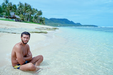 Enjoying suntan and vacation.Young bearded man ralaxing on the tropical sand beach.