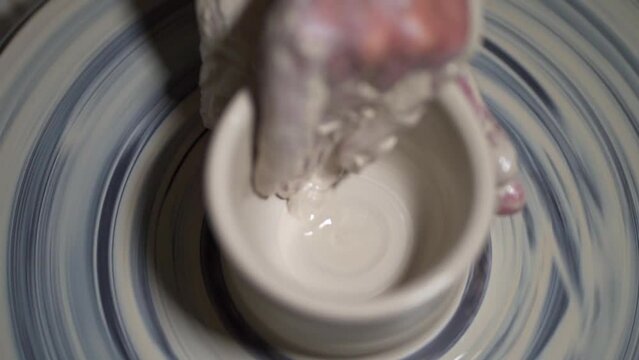Cinematic shot of pottery class, person is forming the cup shape while it spins.