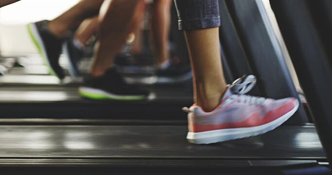 Shoes of an active and fit group of athletes running on a treadmill at the gym or health club. Closeup of athletic people jogging and training their cardio or fitness using workout equipment