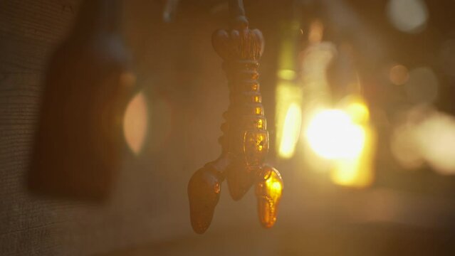 A small decorative lobster hands from a ledge, next to beer bottle decorations. Sun sets in the background casting beautiful golden hour lens flare. Establishing shot.