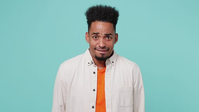 Young man of African American ethnicity wear shirt t-shirt spread hand shrugging shoulders look puzzled have no idea nothing to say I don't know why isolated on plain pastel light blue cyan background