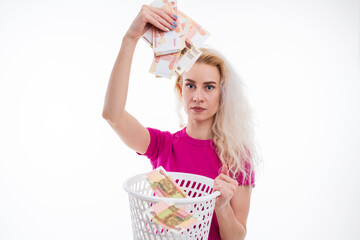 A young woman in a pink T-shirt throws Russian banknotes in the trash on a white background. The...
