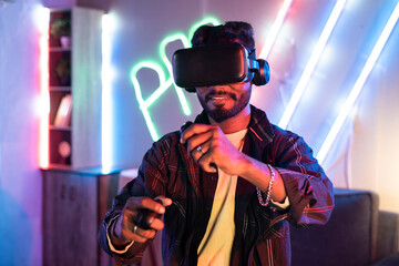 Young man on neon background playing video game virtual reality or VR headset at home using...