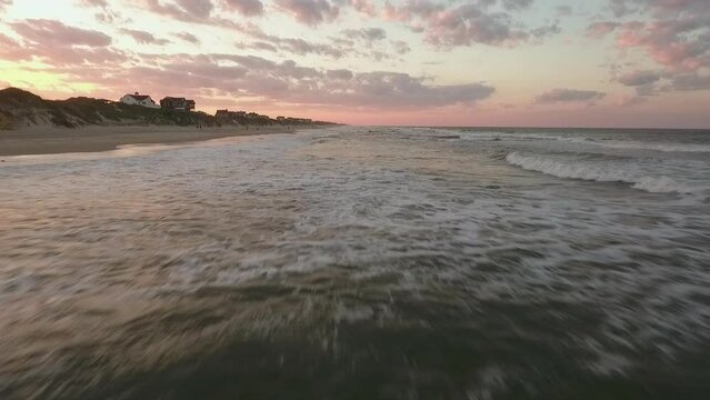 Cinematic drone shot starting low on the ocean then rising to reveal beach homes on the coast of North Carolina