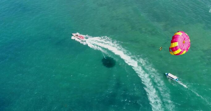 Aerial shot of a parasailing boat going over turquoise water
