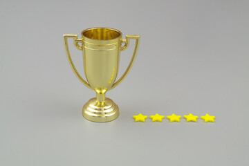 Gold trophy cup with five stars on gray background.