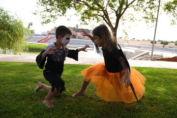 A girl dressed as a witch with an orange skirt and black wings and a boy dressed as a zombie scare the camera at a Halloween party. Trick or treat. 31st October. Happy halloween.