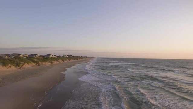 Drone shot of beach with waves crashing and then rising to show houses on the coast on the outer banks of North Carolina