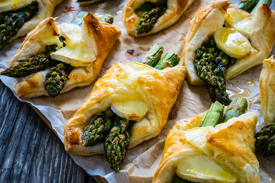 Baked puff pastry with asparagus and cheese on baking paper on wooden table