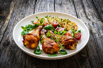 Barbecue chicken drumsticks with fried potato, lettuce and mini tomatoes on wooden table
