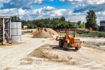 A large front loader transports materials in a concrete production plant. Production of concrete. Transportation of bulk materials. Construction equipment. Bulk cargo transportation.