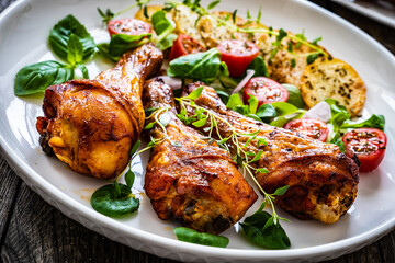 Barbecue chicken drumsticks with fried potato, lettuce and mini tomatoes on wooden table
