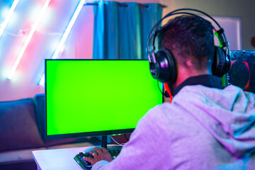 shoulder shot of professional gamer playing live video game on green screen monitor by talkng on headphones - concept of entertainment, excitement and cyberspace. © WESTOCK