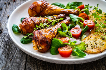 Barbecue chicken drumsticks with fried potato, lettuce and mini tomatoes on wooden table
