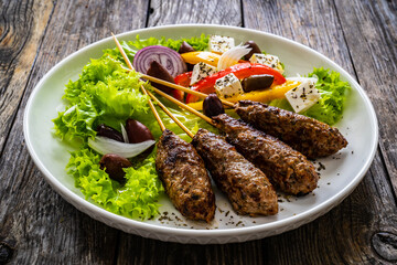 Souvlaki - greek shashlik served with fresh green vegetables and feta cheese on wooden table
