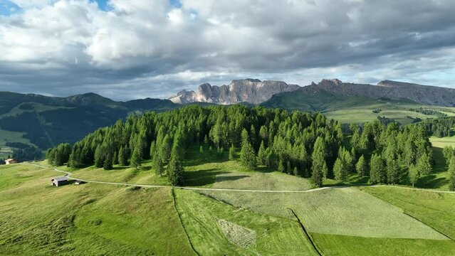 Amazing view on Dolomites peak with a hiking path leading to the mountains. Sunrise drone shot of idyllic Alpe di Suisi mountains in South Tyrol. Wooden cottages at sunrise.