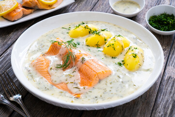 Roasted trout fillet with potatoes and dill sauce served on wooden table
