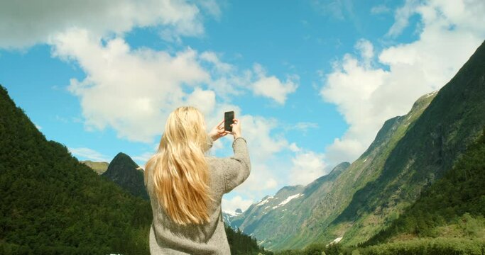 Female travel researcher and biologist taking a phone picture of a green mountain view in nature. Back view of ecologist alone doing research outdoors. Woman looking at mountains and taking photos