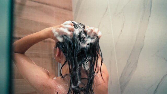 Handheld cinematic backshot of a young woman washing her hair with shampoo