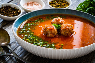 Tomato soup with pork meatballs and fresh parsley on wooden table
