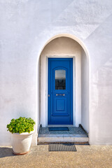 Traditional blue door and whitewashed walls of Greek house entrance and flower pot with rich foliage. Midday, summer sunshine, Milos, Greece