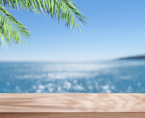 Empty table top under palm leaves and blurred sparkling sea at the background. Place for your product or brand name display.