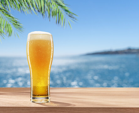 Glass of chilled beer on table and blurred sparkling sea at the background. Place for your product or brand name display.