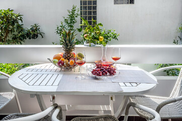 Balcony with furniture, white table served with fruit basket and wine glasses,  four chairs, sunny summer day, holiday concept. 